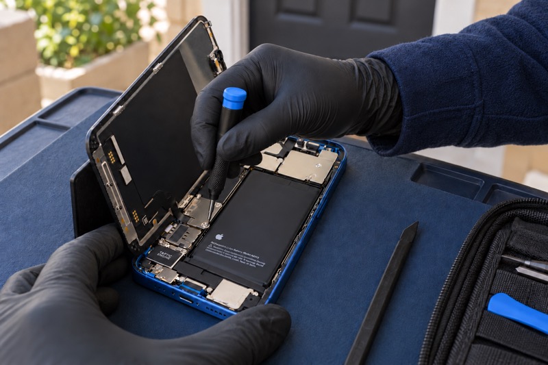 An iPhone screen lifted open while a screw is removed, outside a home.